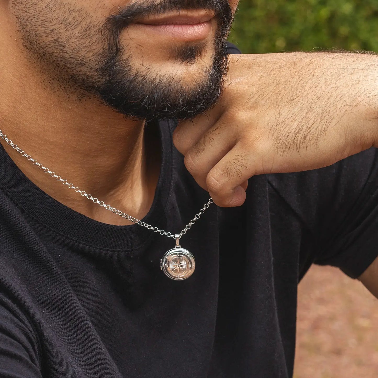 Man wearing a black shirt with a silver necklace featuring a round compass pendant.
