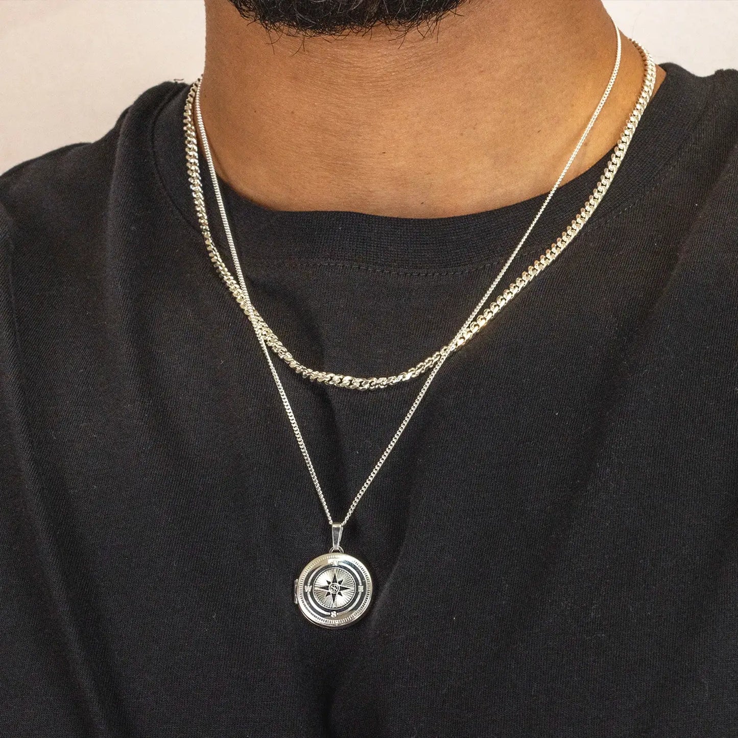 Man wearing a black shirt with a silver necklace featuring a compass pendant.