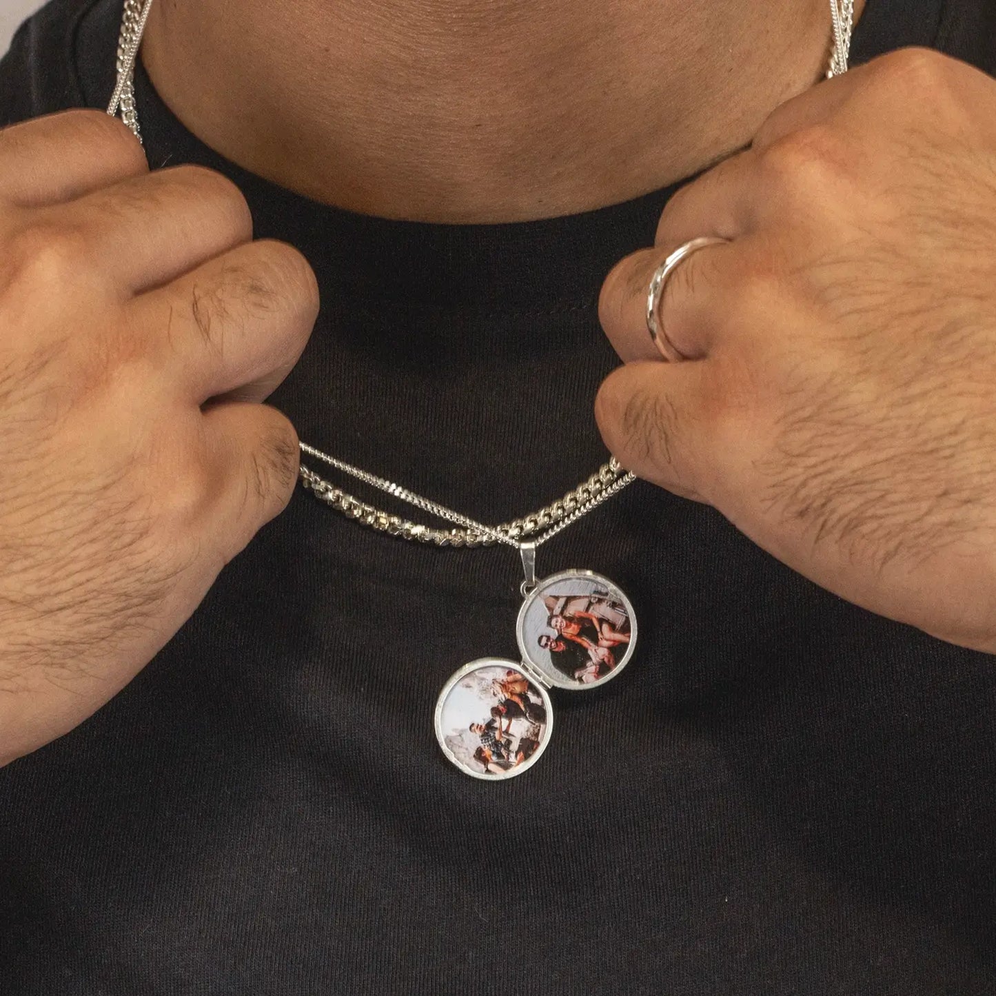 man wearing a silver chain necklace with two photos inside on a black t-shirt