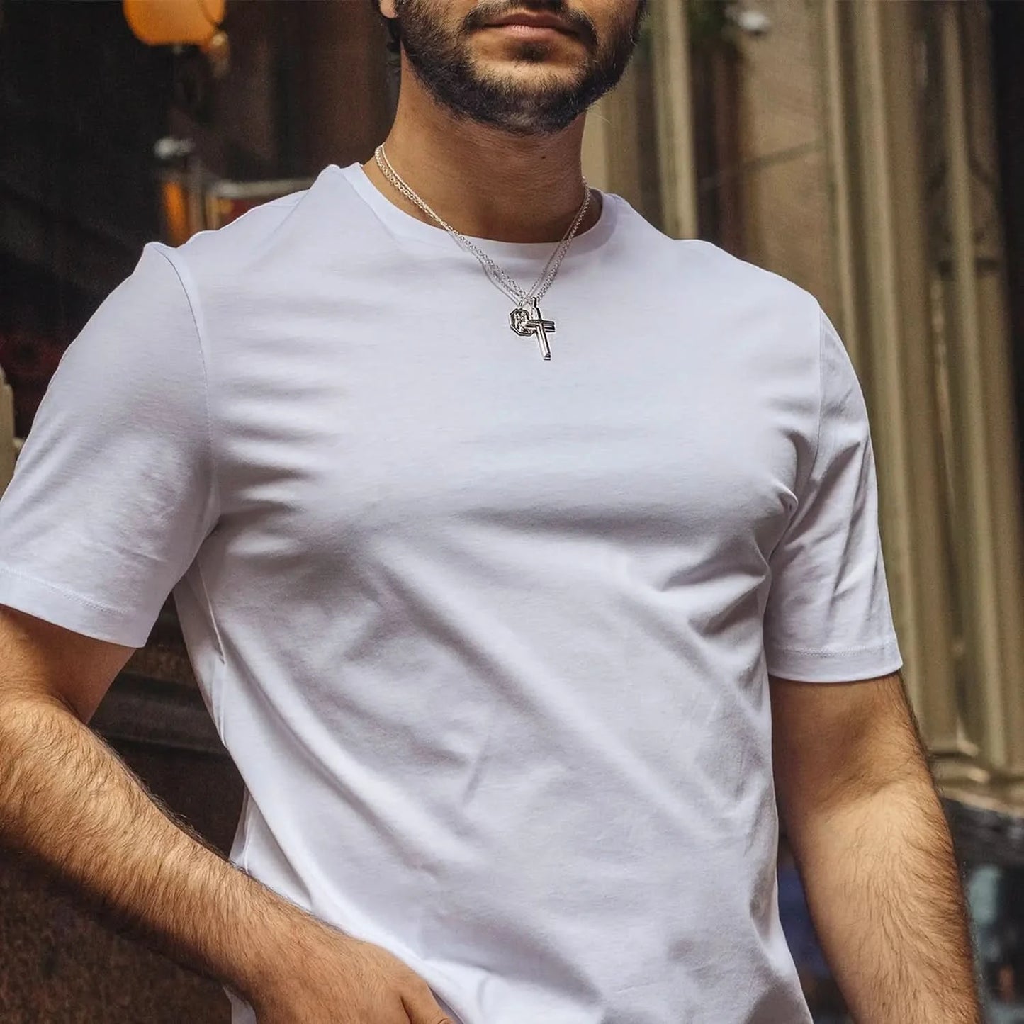wide view photograph of a heavy weight silver cross necklace on a belcher chain, worn by a male model wearing a white t-shirt