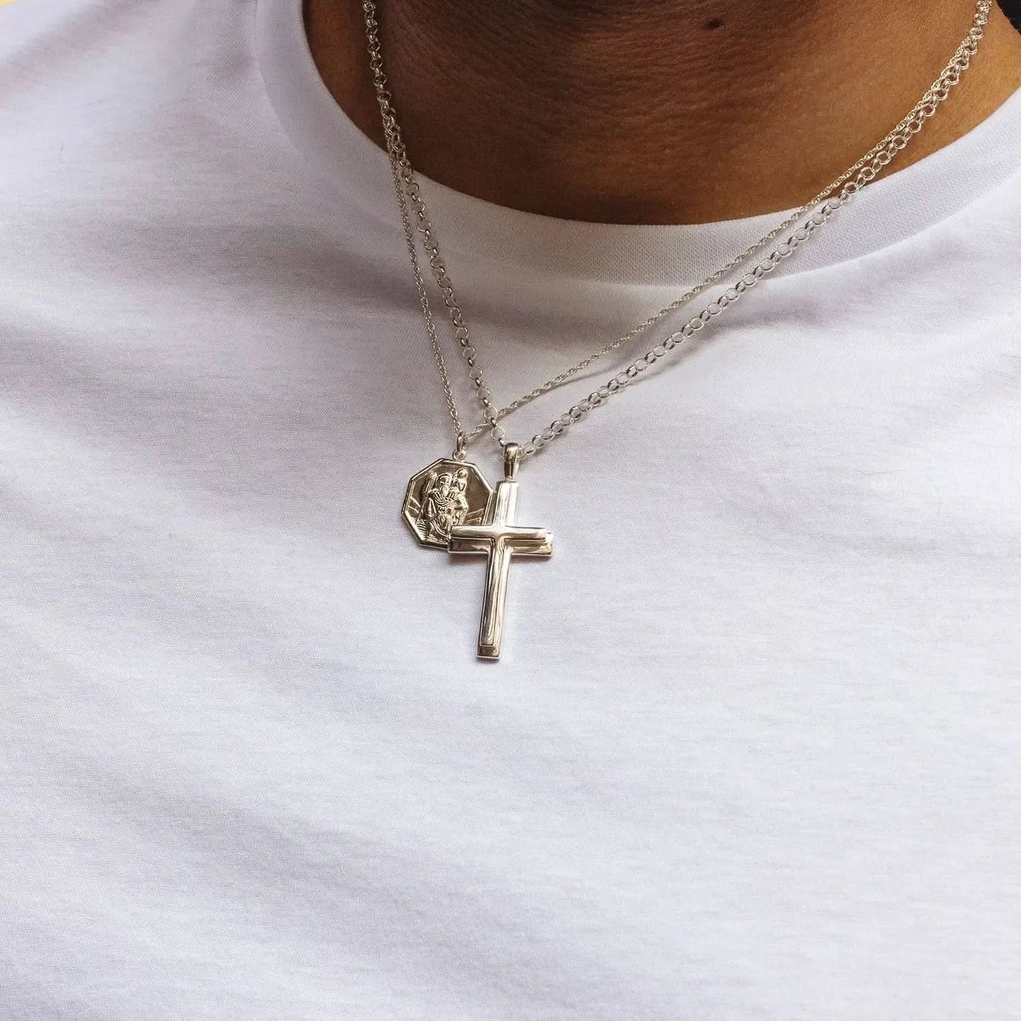 close up photograph of a heavy weight silver cross necklace on a belcher chain, and a st Christopher silver necklace, both worn by a male model wearing a white t-shirt