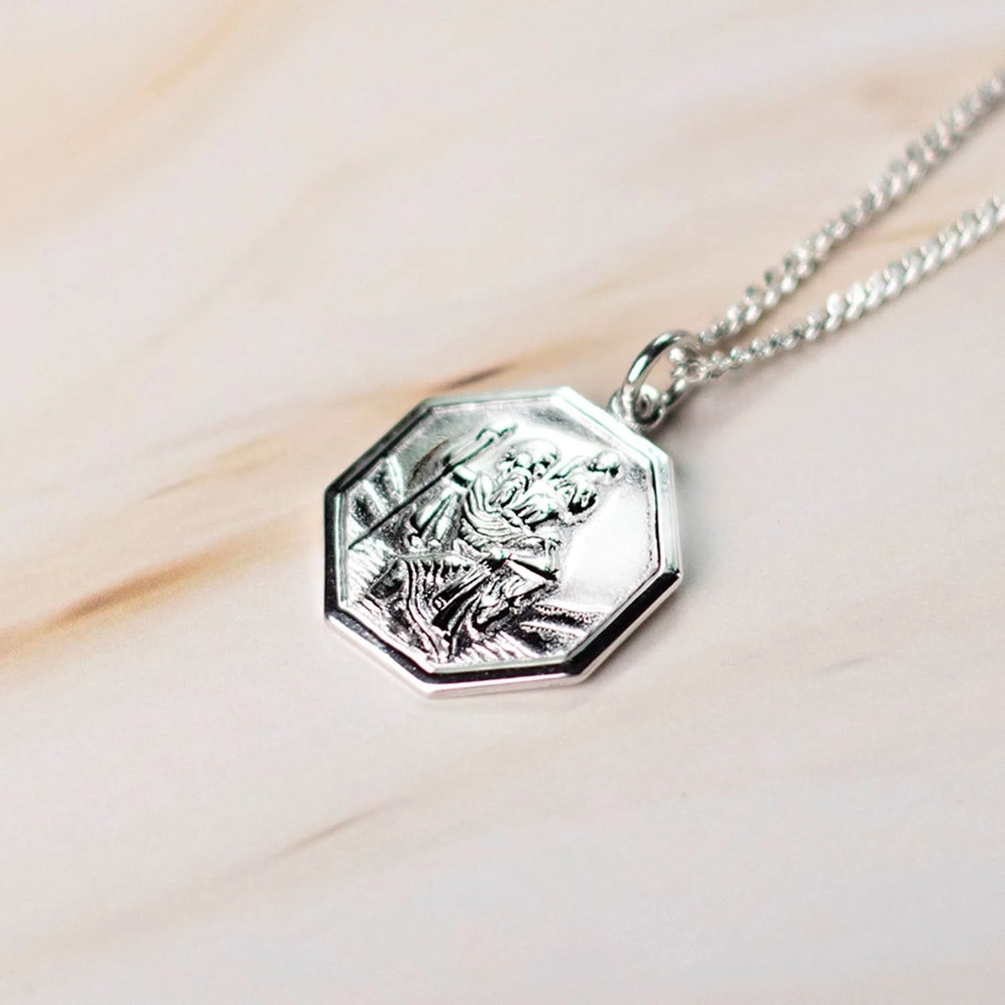 Close-up of white gold St. Christopher octagon pendant on curb chain against a marble background
