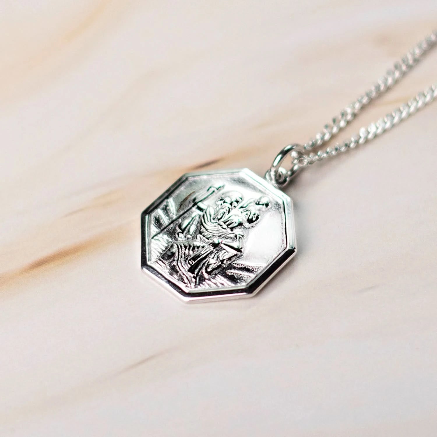 Close-up of white gold St. Christopher octagon pendant on curb chain against a marble background