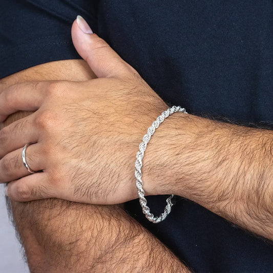 Close-up of a man’s wrist wearing a sterling silver rope chain bracelet, paired with a simple silver ring.
