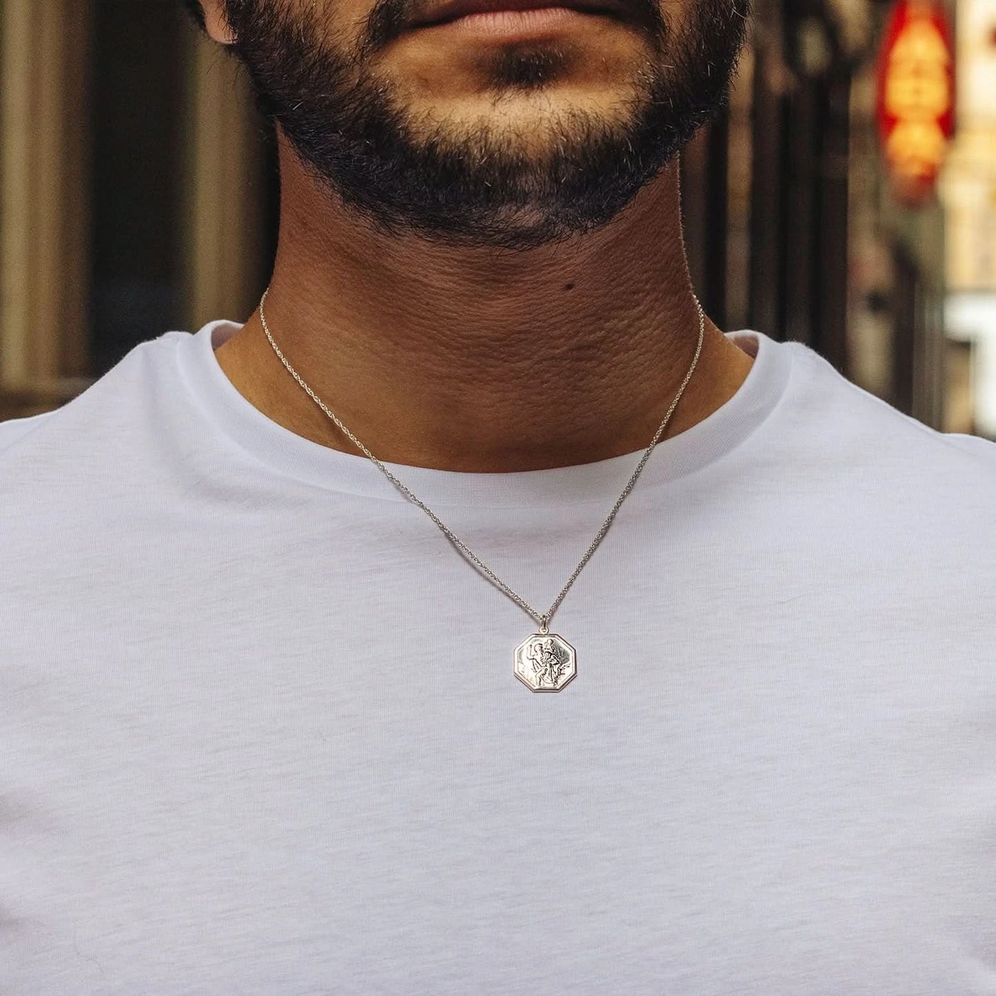 Man wearing octagonal white gold St. Christopher medal necklace over white t-shirt