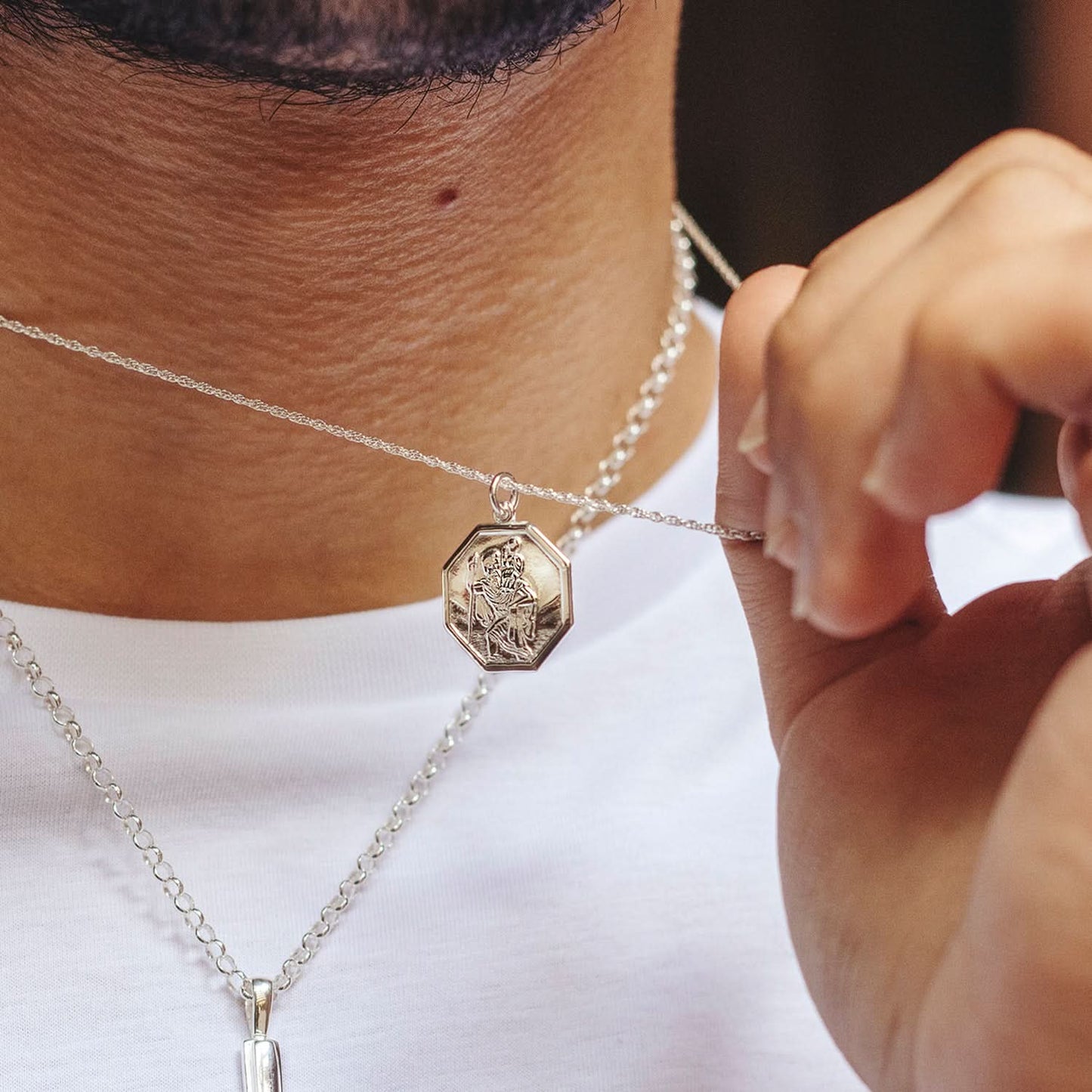 Man wearing white gold St. Christopher pendant necklace, holding charm close-up
