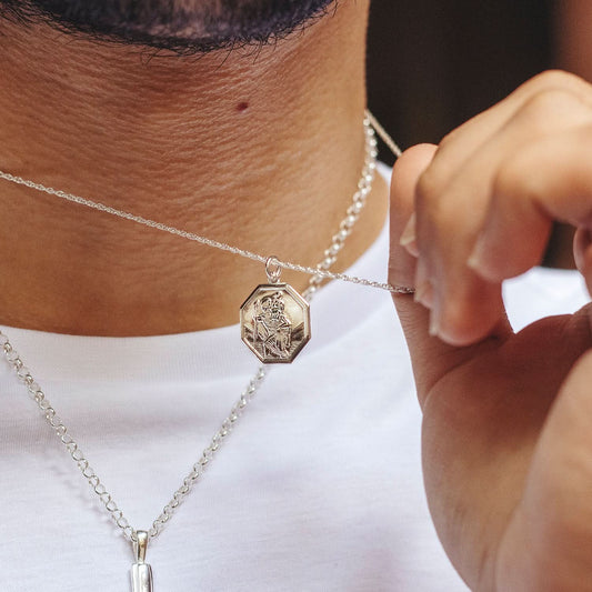 Man wearing white gold St. Christopher pendant necklace, holding charm close-up