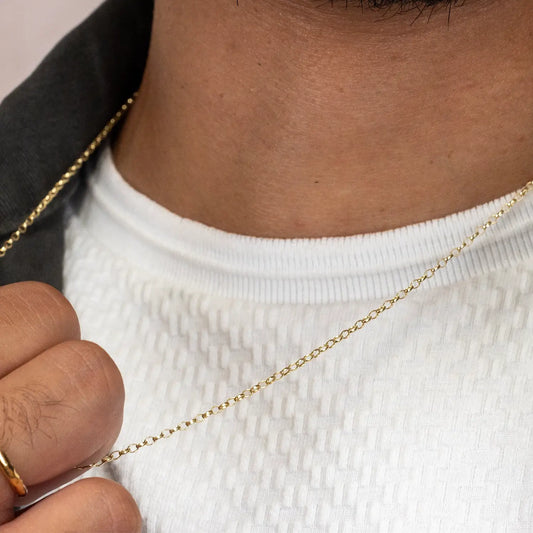 Close-up of a solid gold belcher chain held by a hand against a neutral background