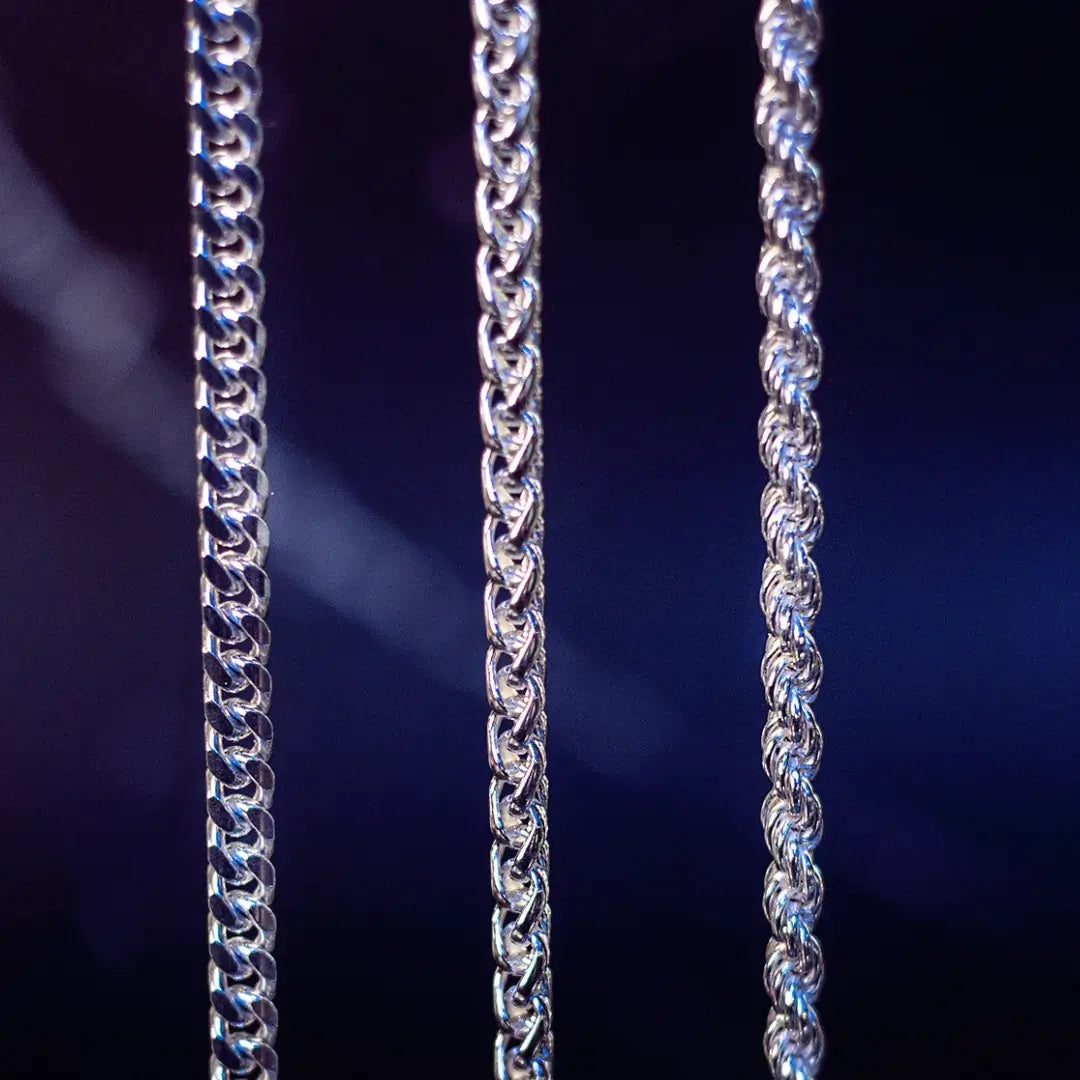 Close-up of three sterling silver chains showing different link styles against a dark blue background.