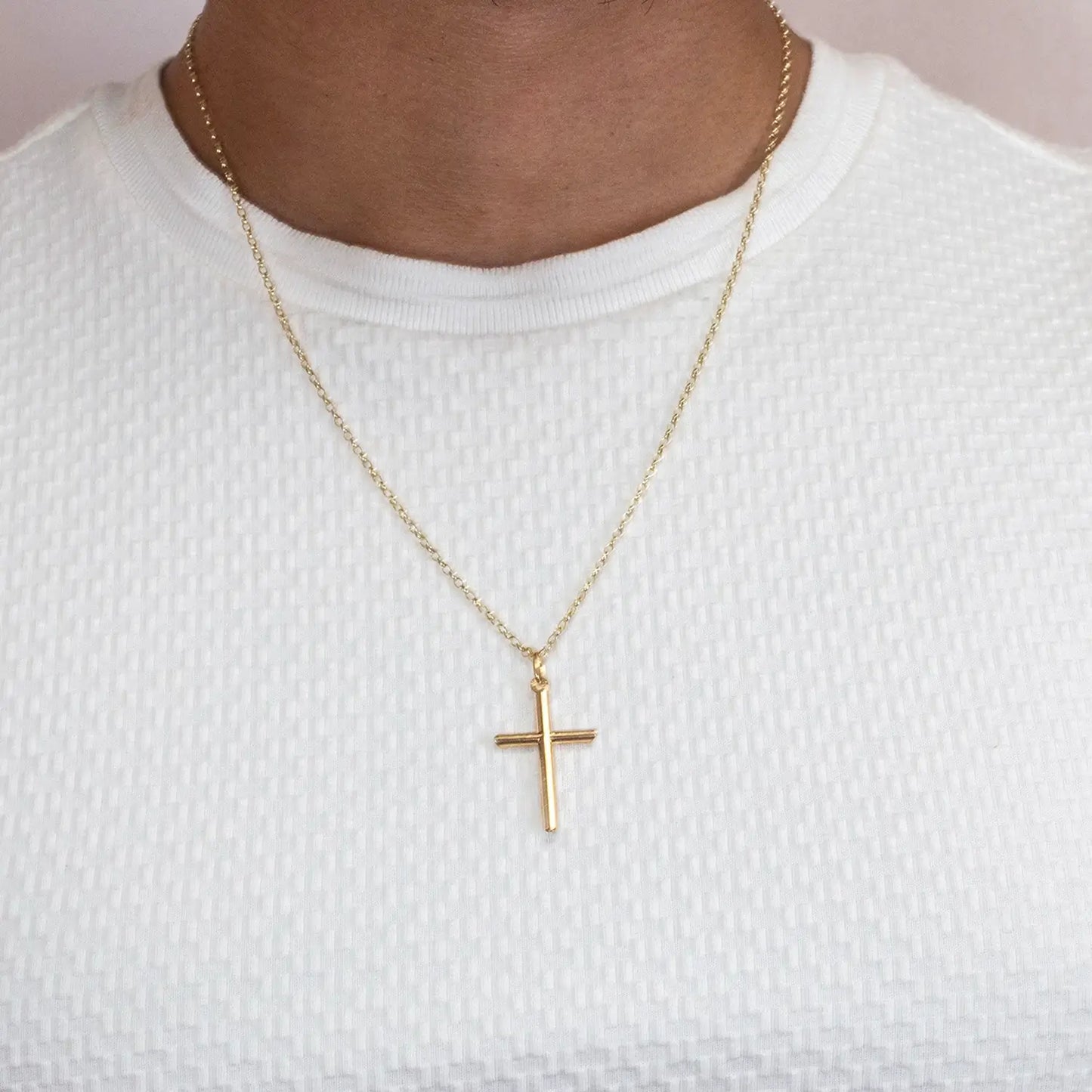 Gold cross necklace on a person wearing a white shirt