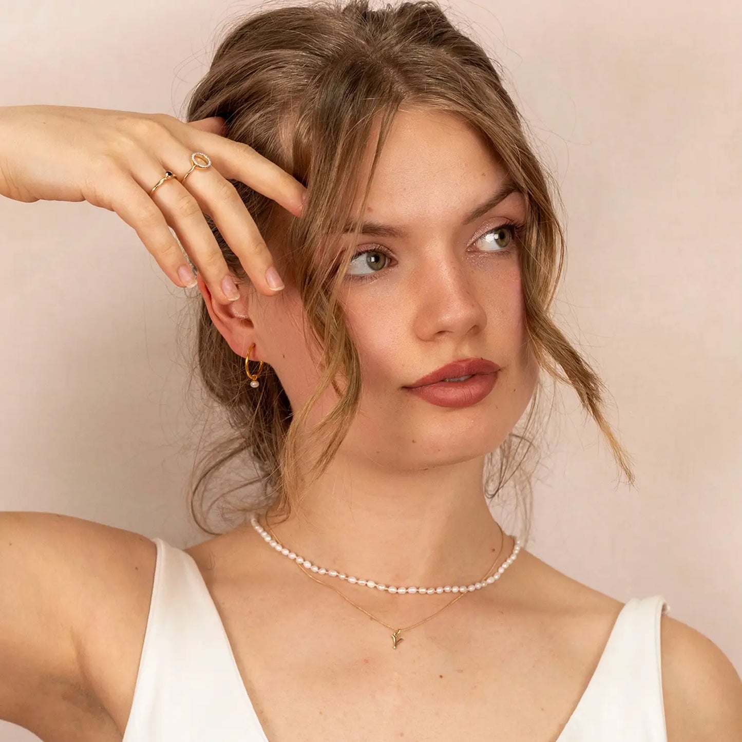 Head and neck shot of a female model wearing a white strapless dress, the 9-carat solid gold initial necklace, letter 'Y', on a close curb chain and a separate necklace of seed pearls.