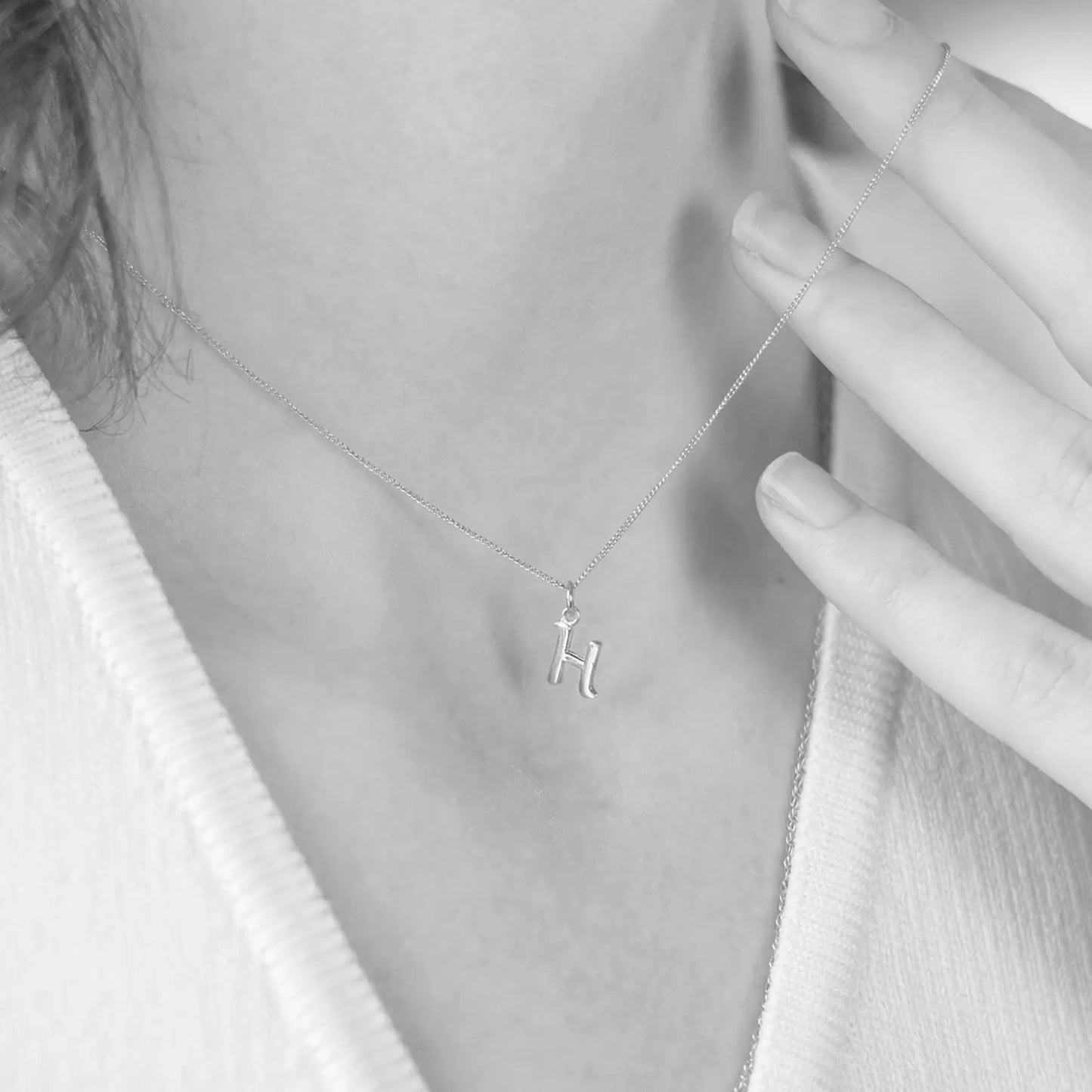 Person wearing a white gold necklace with a 'H' pendant, close-up of the necklace.