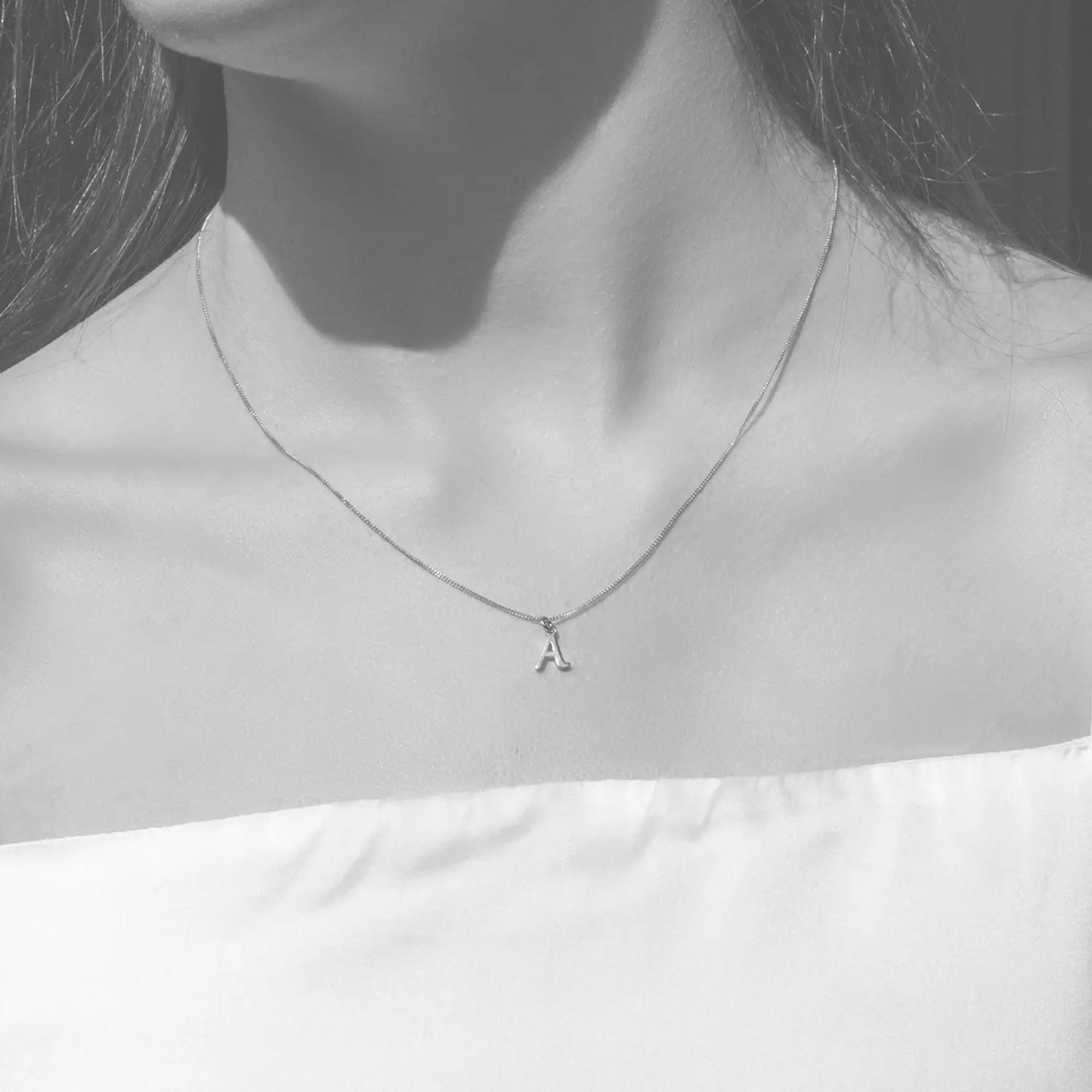 white gold Necklace with a small letter 'A' pendant worn by a person on a plain background