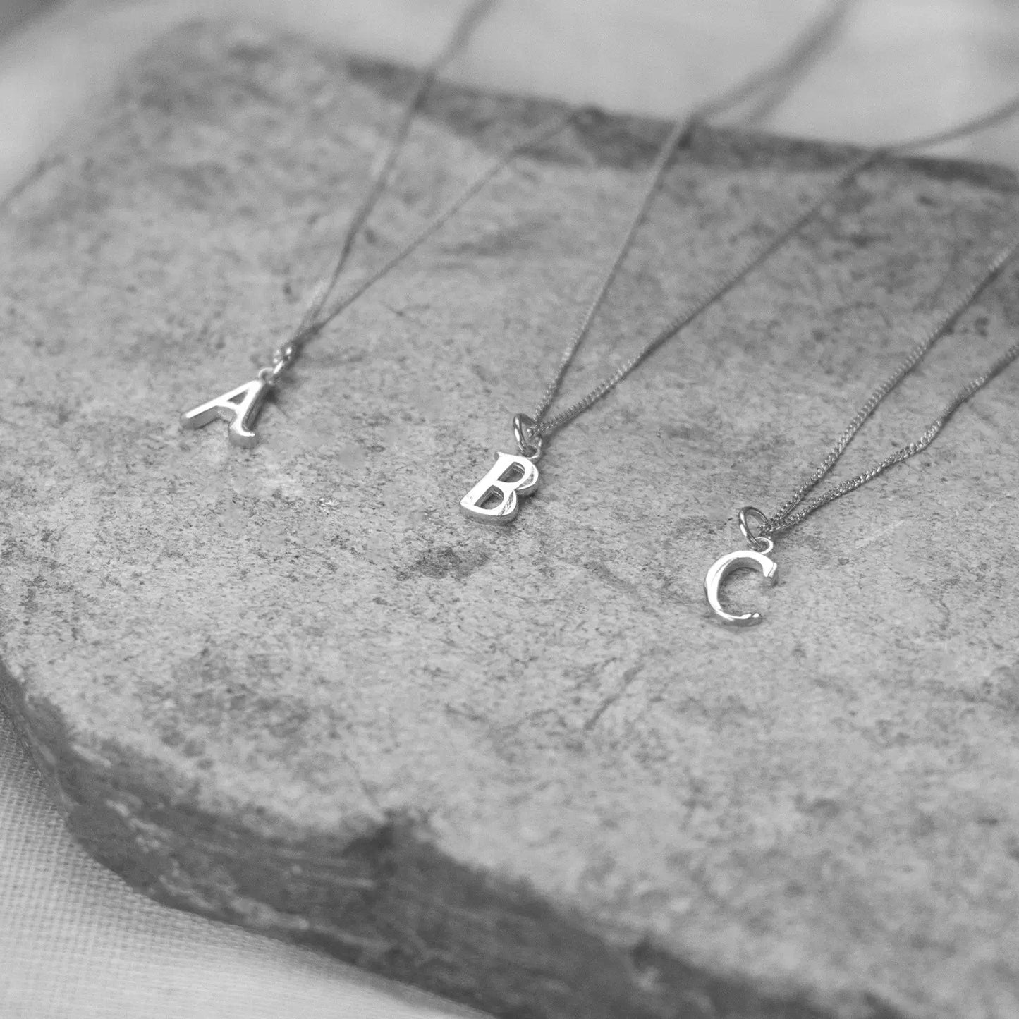 Three white gold necklaces with letter pendants on a stone surface