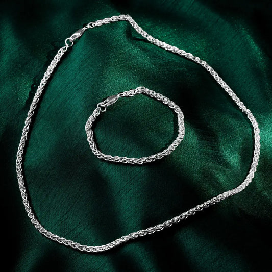Silver spiga-style necklace and matching bracelet displayed on dark green satin fabric.