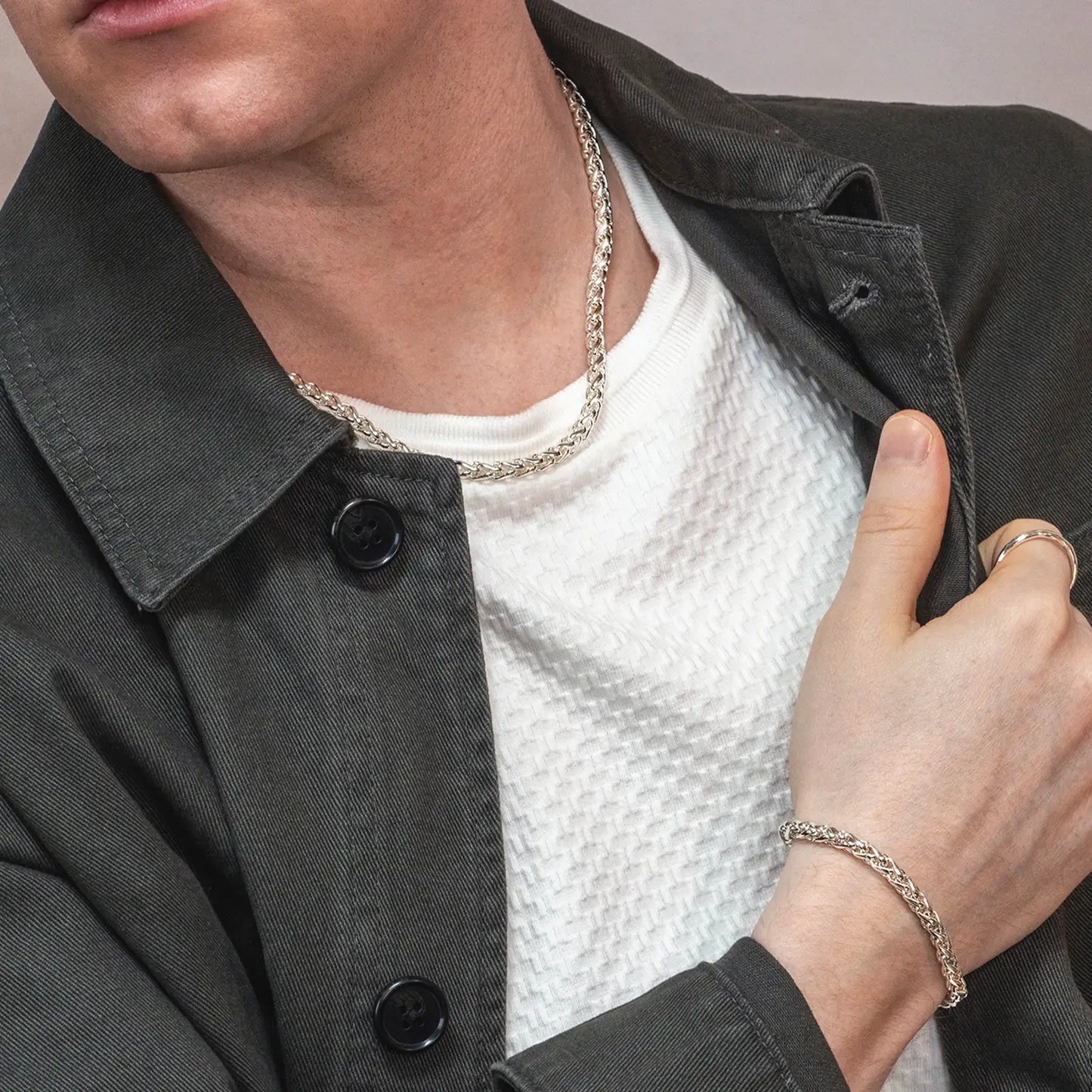 Person wearing a sterling silver heavyweight men's Spiga chain necklace and bracelet with a black jacket and white shirt.