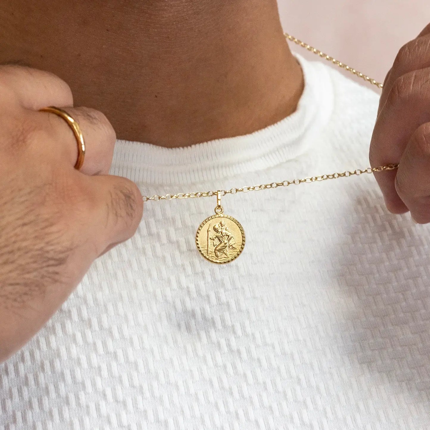 Gold st christophernecklace with a pendant being adjusted on a white shirt