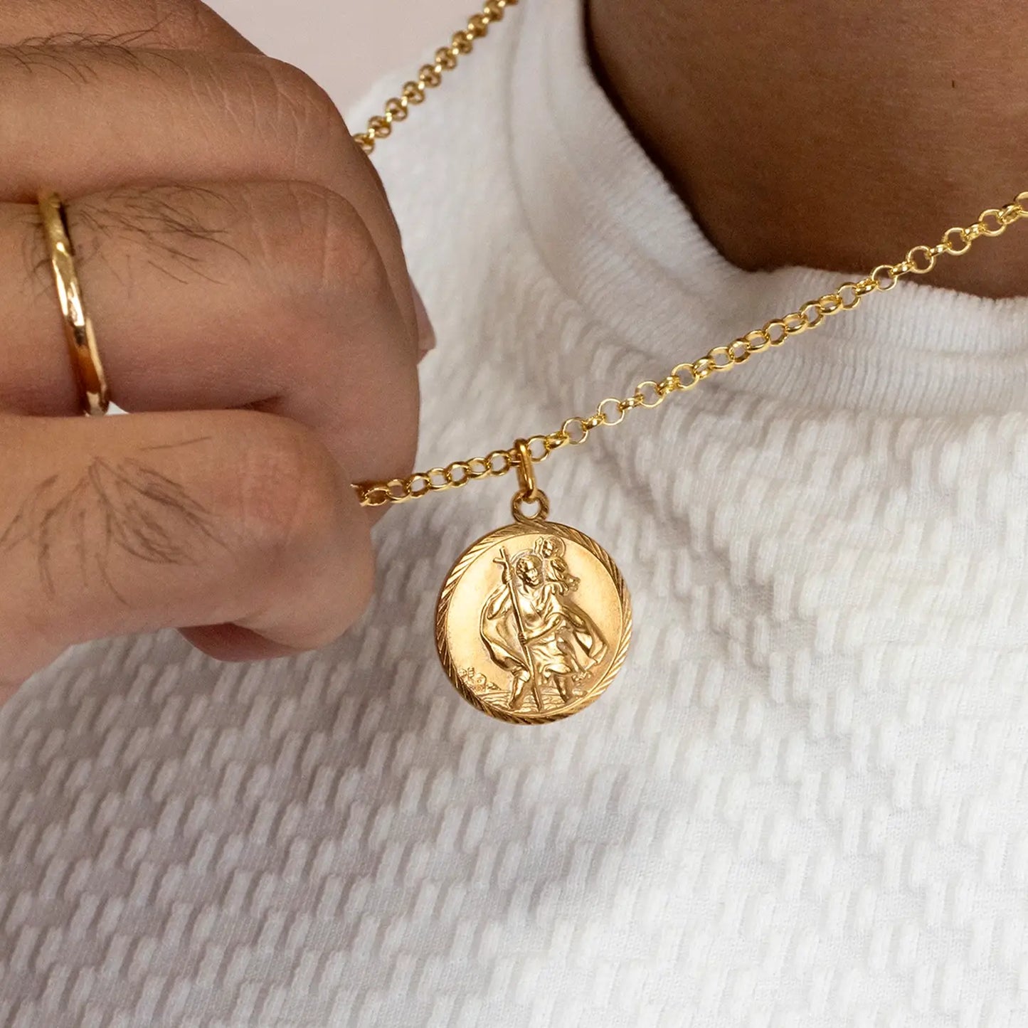 Gold st Christopher necklace with a pendant held by a hand on a neutral background