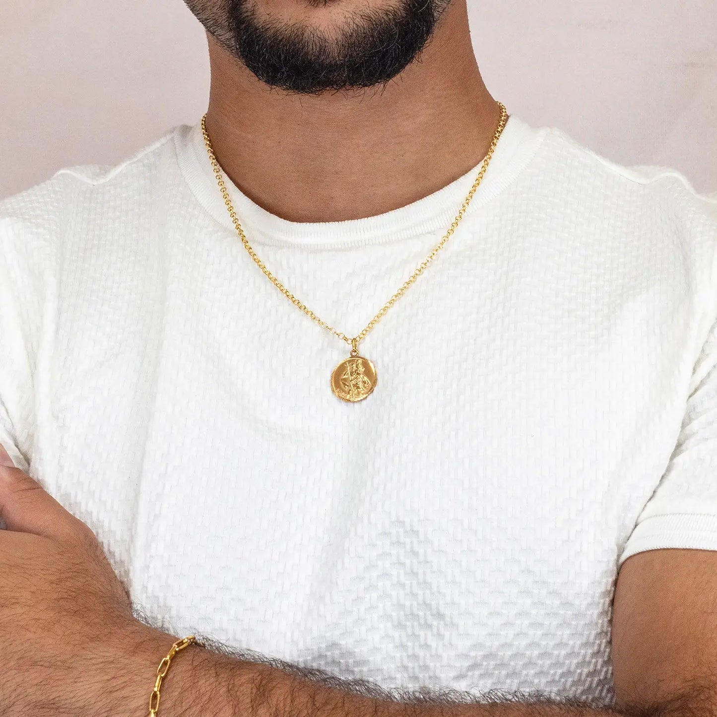Man wearing a gold st Christopher necklace with a pendant on a plain background