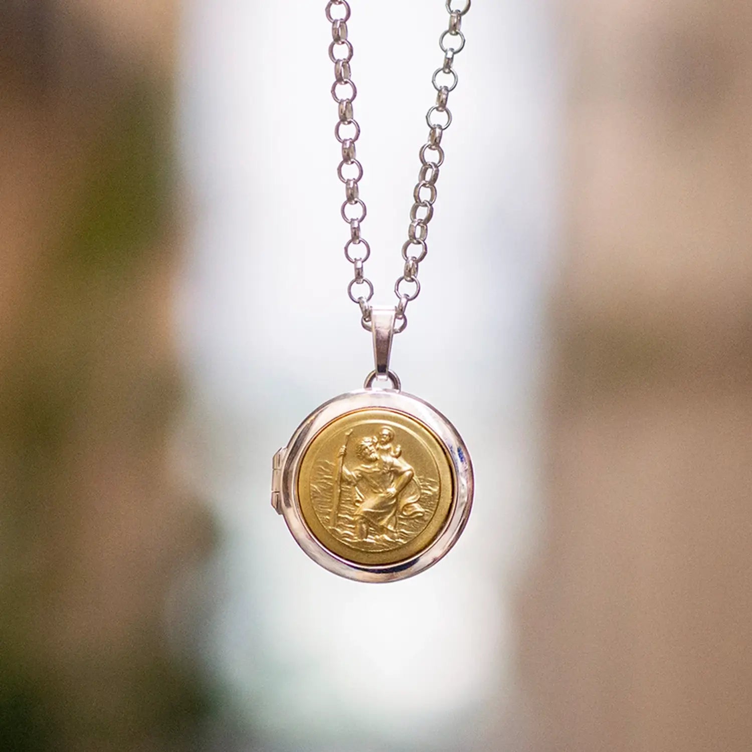 photograph of a silver and gold st Christopher locket from the front hanging on a silver chain and on an Italian street