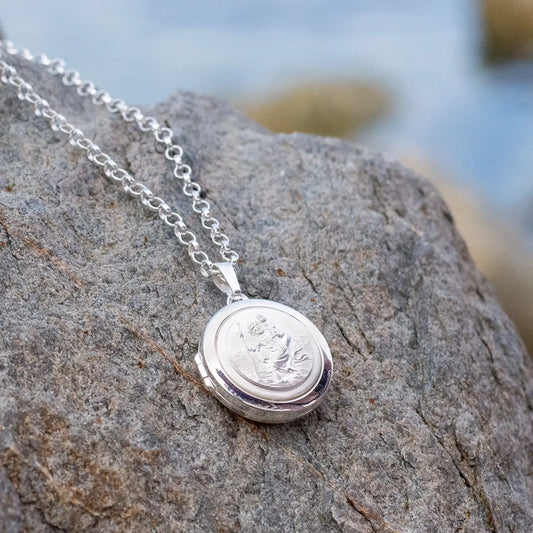 photograph of st christopher locket in silver lying against a rock with a beach in the background