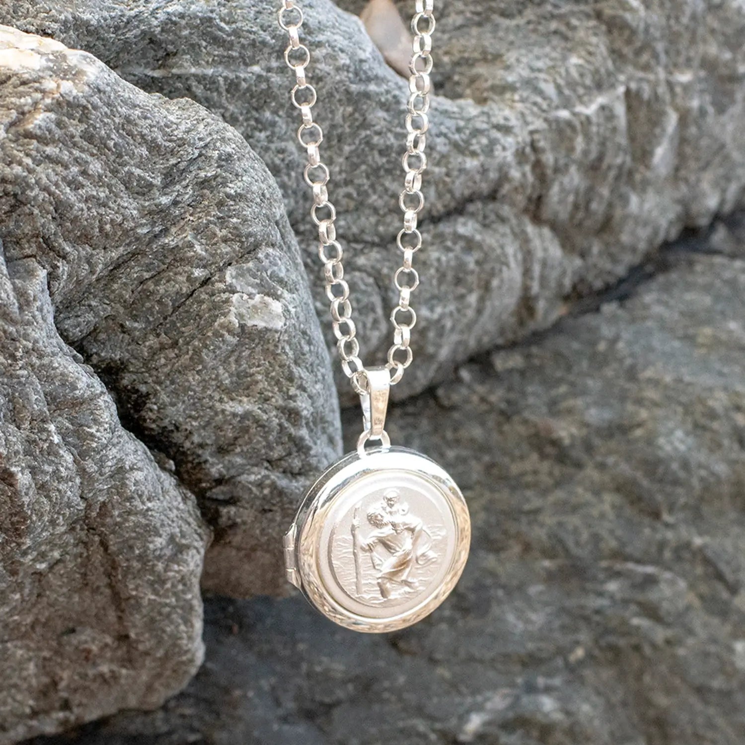 photograph of st christopher locket in silver lying against a rock on a belcher chain