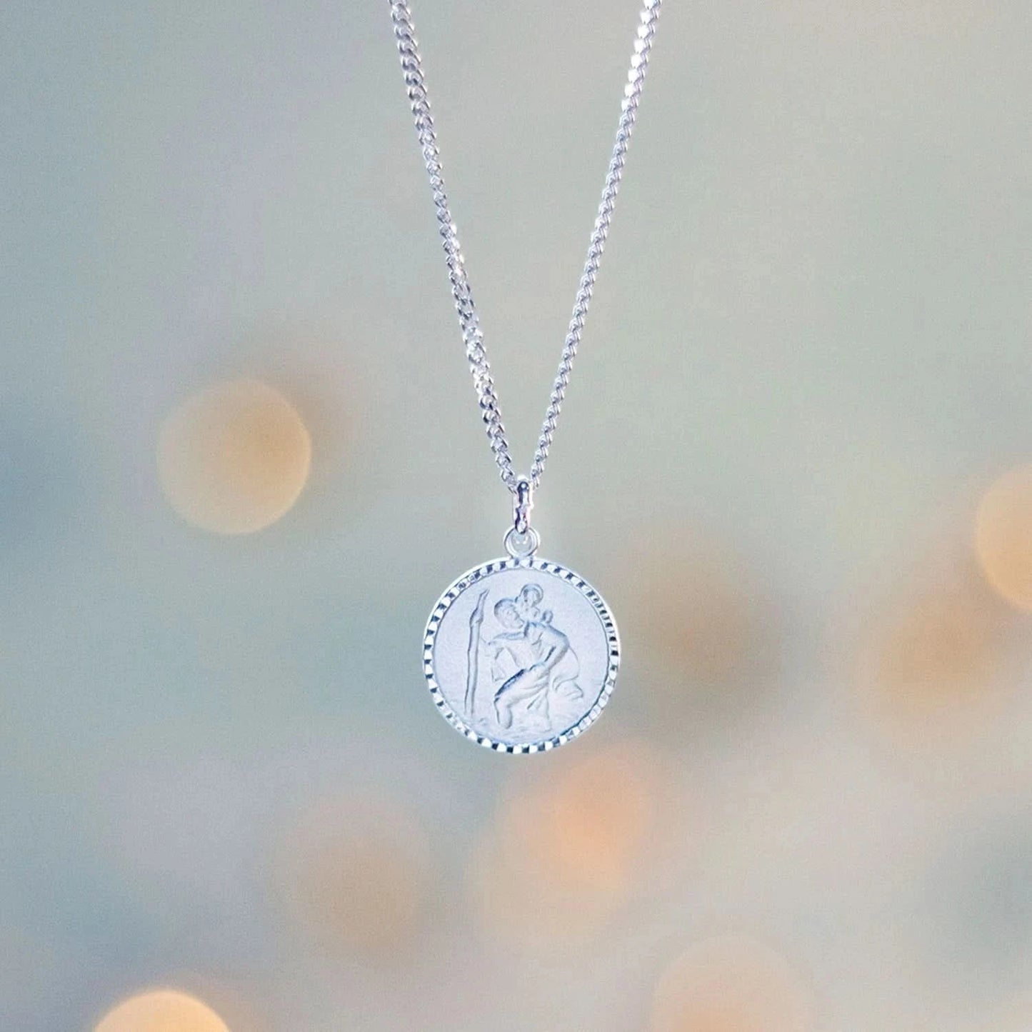 photograph of a round st Christopher necklace in silver on a curb chain, against a blue background