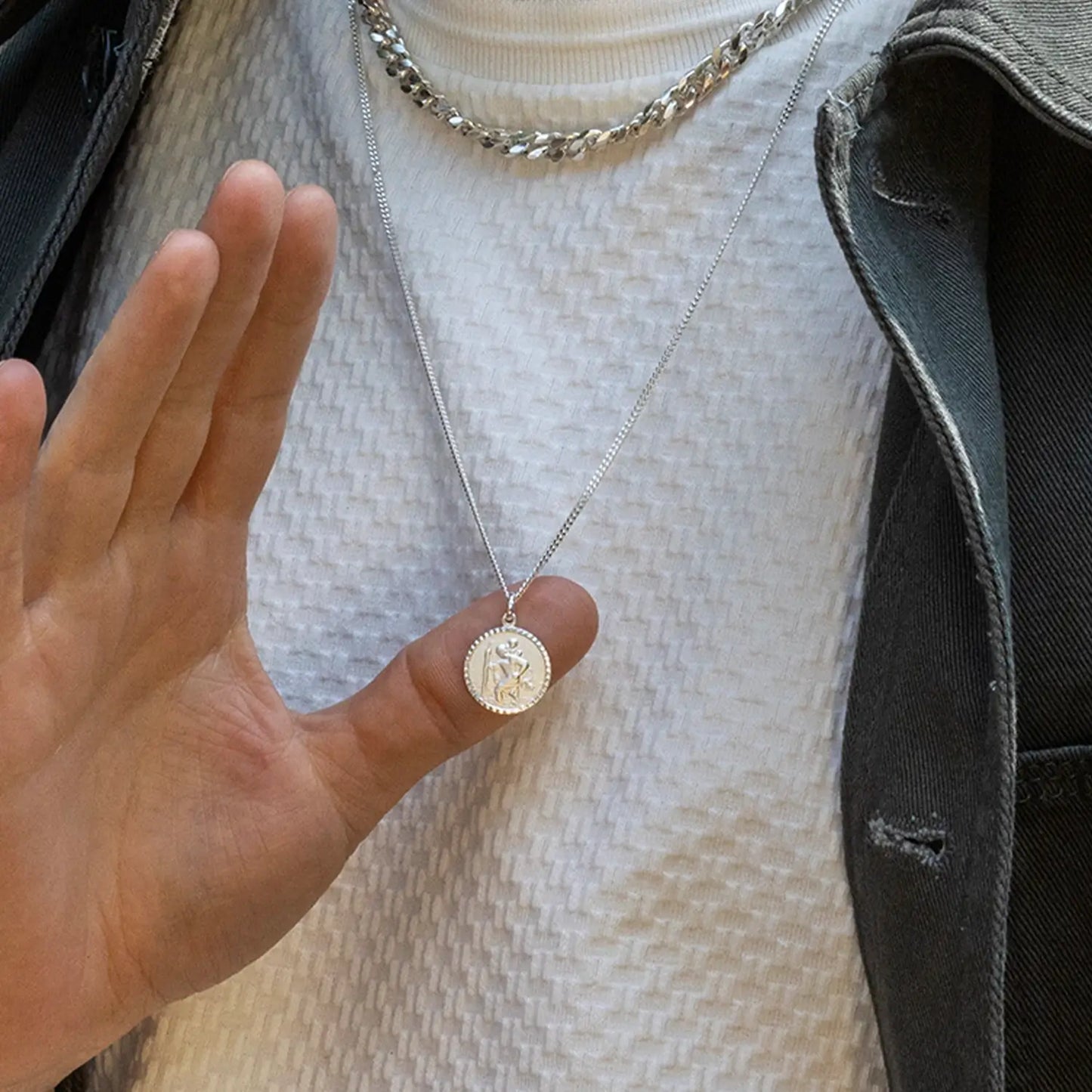 man wearing a silver st Christopher necklace with a pendant, held up by a hand.