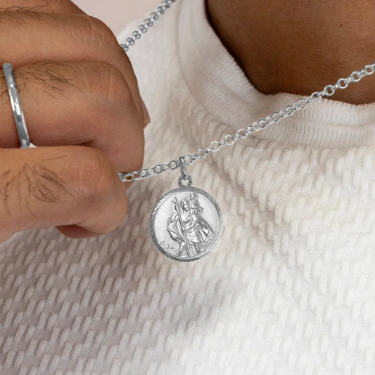 Silver st Christopher necklace with a round pendant held by a hand on a light fabric background
