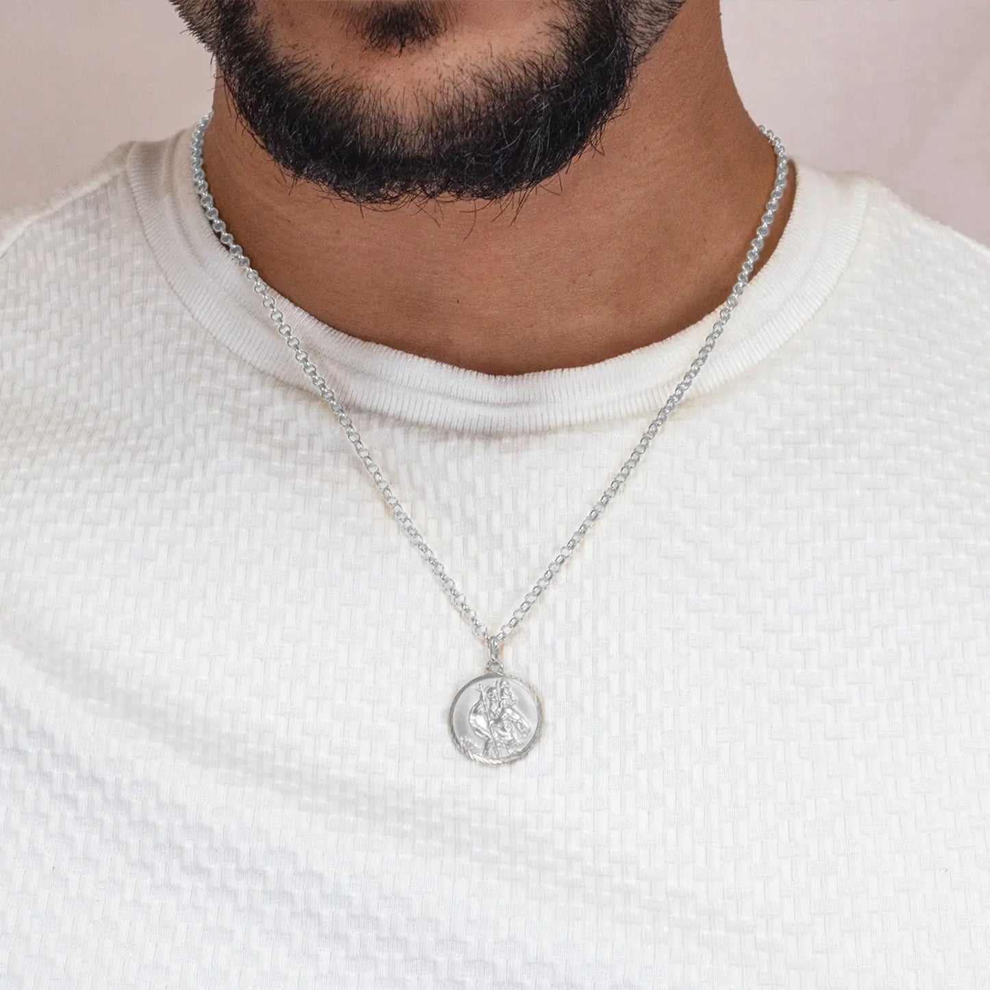 Man wearing a silver st Christopher necklace with a pendant on a plain background