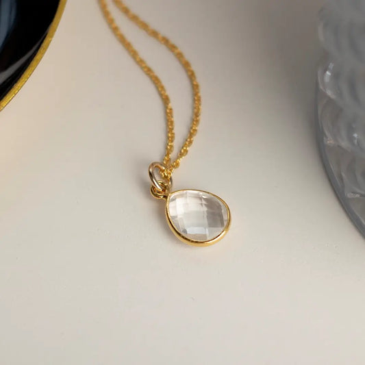 White quartz teardrop charm pendant set in gold on a delicate gold chain, photographed on a neutral background.