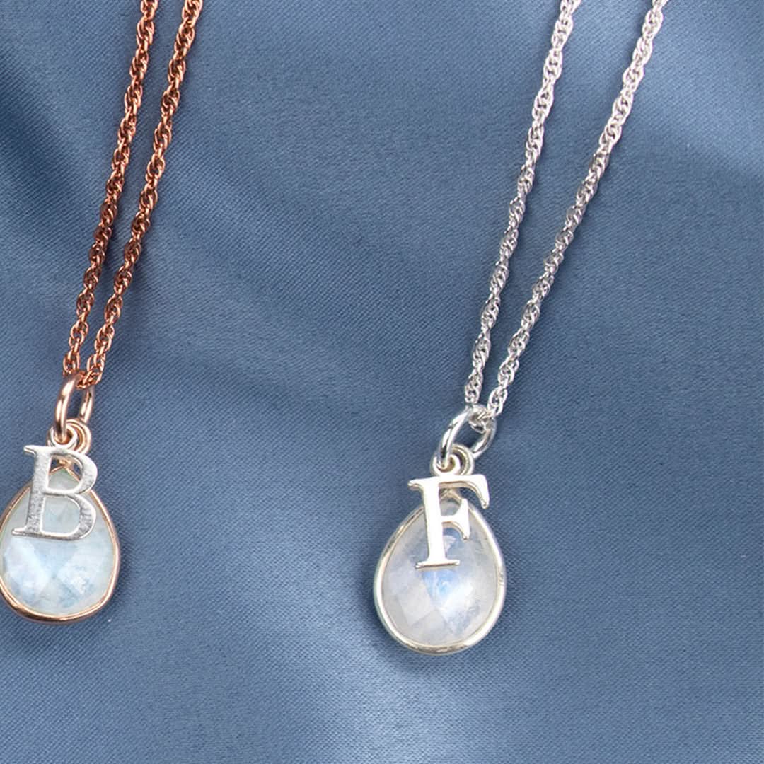 two moonstone charm necklaces with silver initial charms on a white background