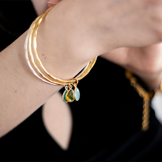 close up of models arm wearing three charm bangles with birthstones
