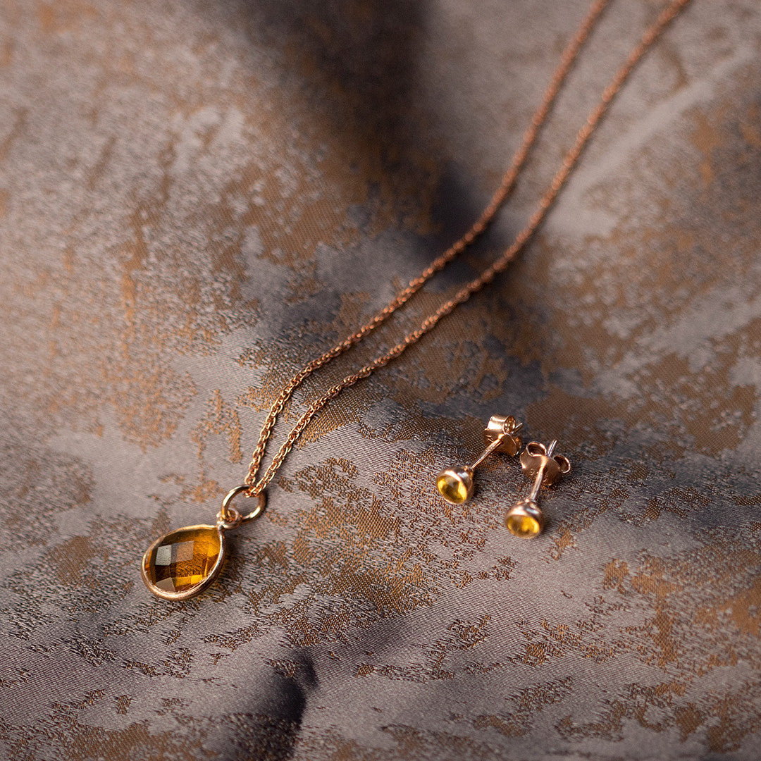 citrine mini stud earrings and charm necklace in rose gold on a piece of fabric 