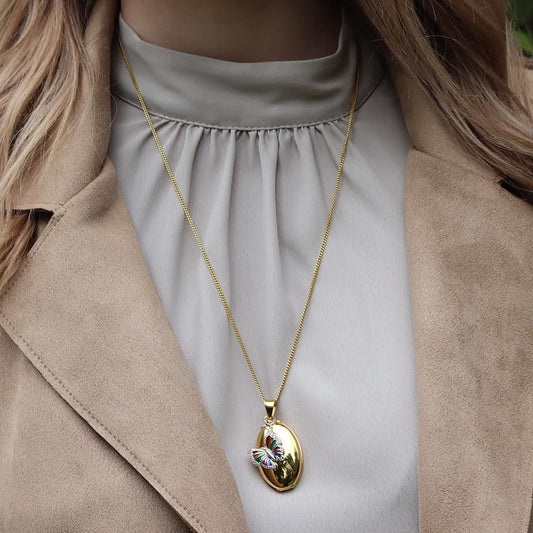 model wearing gold curb chain with gold oval locket with butterfly charm