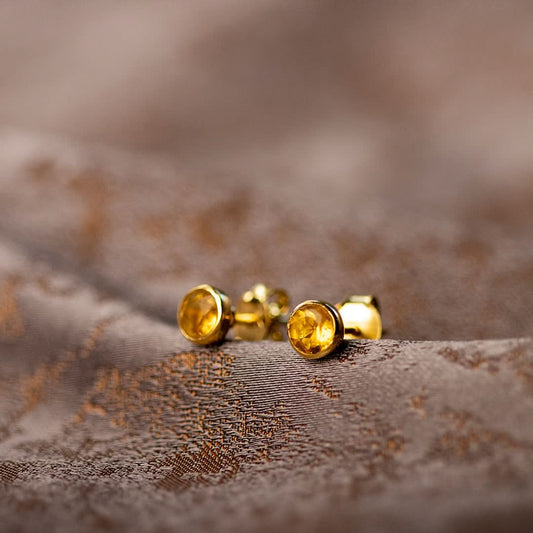 citrine mini stud earrings in gold sitting on a piece of fabric