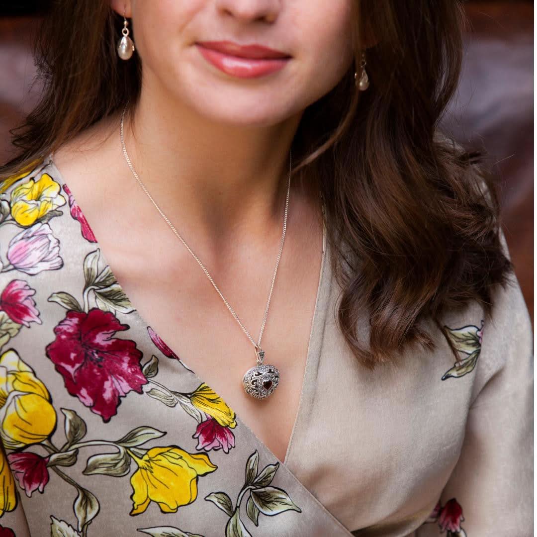 model in flower design top wearing silver vintage heart locket with garnet gem stone