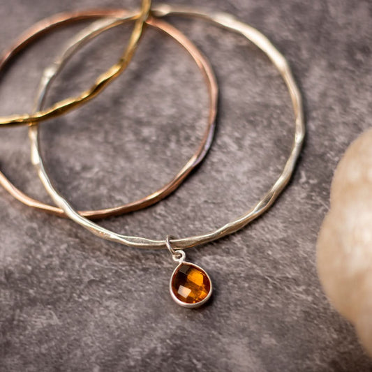 close up of three charm bangles in gold, silver and rose gold on a piece of grey fabric