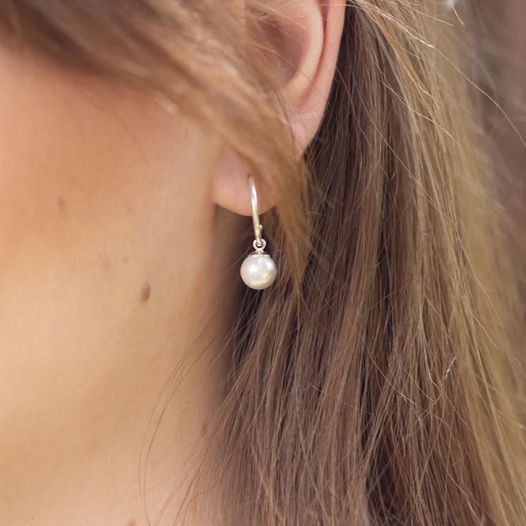 close up of model wearing round pearl drop hoop earrings in ivory silver