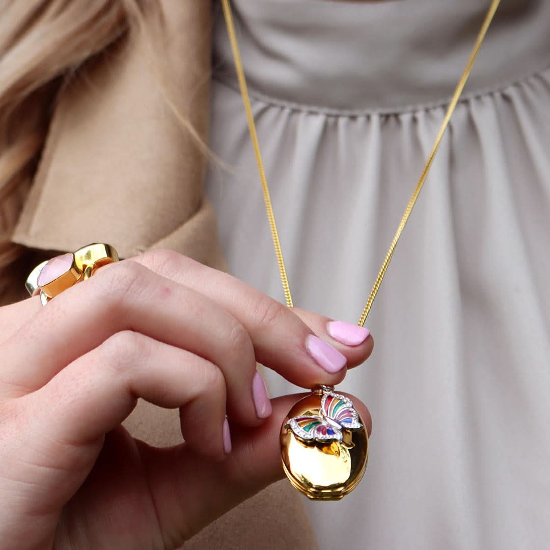 model wearing gold curb chain with gold oval locket with butterfly charm