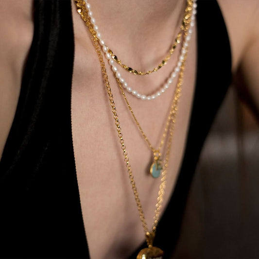 Layered gold chain necklaces with pearls and pendants worn on neckline