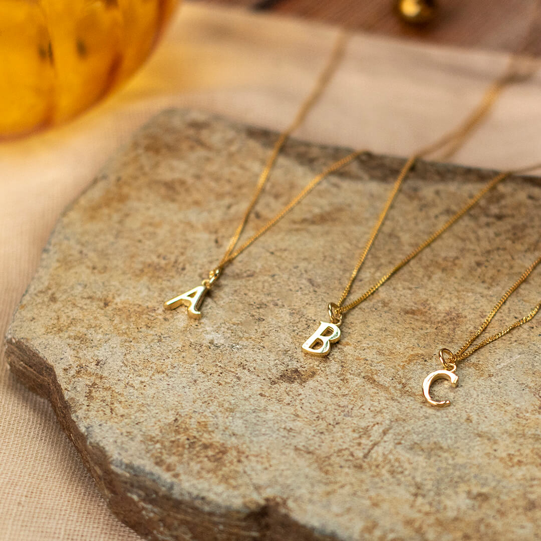 Three diamond disc initial pendants spalling A, B, C displayed on a flat  rock