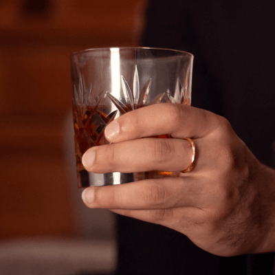 male model holding glass wearing gold band ring 