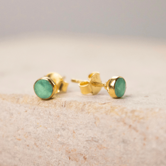 Pair of gold vermeil stud earrings with round green chrysoprase gemstones, displayed on a neutral stone surface.