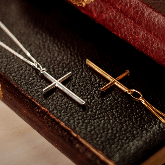 Silver and gold vermeil cross necklaces displayed on a vintage leather book, showcasing minimalist cross pendants on fine chains.