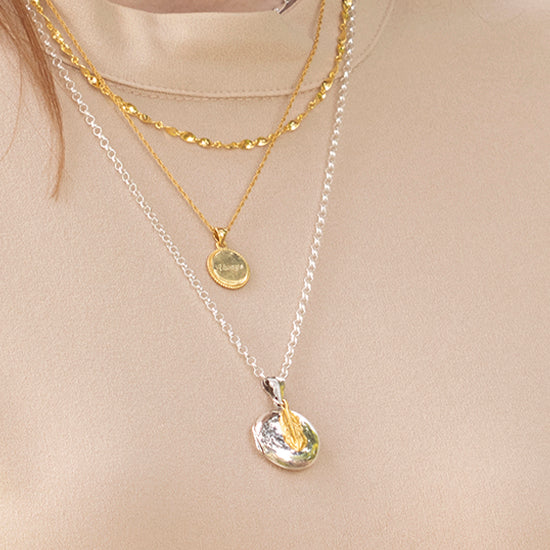 woman wearing a silver locket with a gold feather charm attached