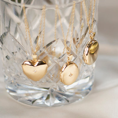Three Lily Blanche Gold Diamond lockets displayed on a crystal glass