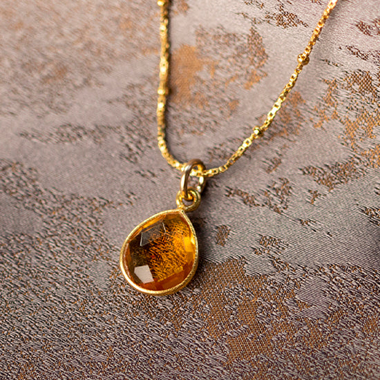 a tear shaped citrine gemstone necklace in gold on a gold chain against a piece of beige fabric