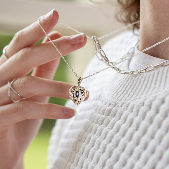photograph of a female hand holding a small, heart shaped silver locket in her hand