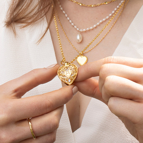 woman holding a gold heart shaped locket with a filigree design